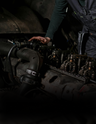 Mechanic inspecting an engine in a dark workshop, hand on exposed machinery.