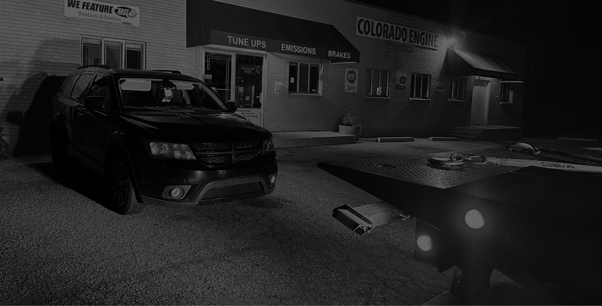 Dark parking lot with two cars parked beside a lit building at night