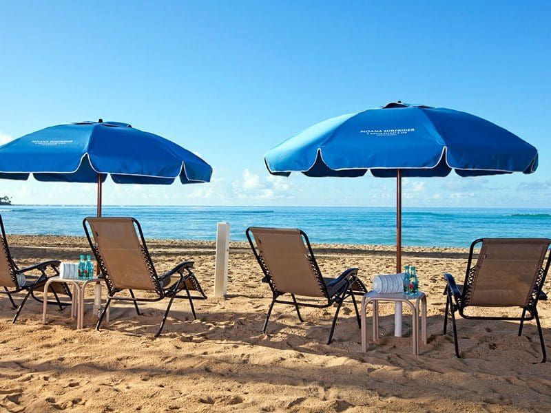 Beach scene with blue umbrellas, lounge chairs, and ocean view.