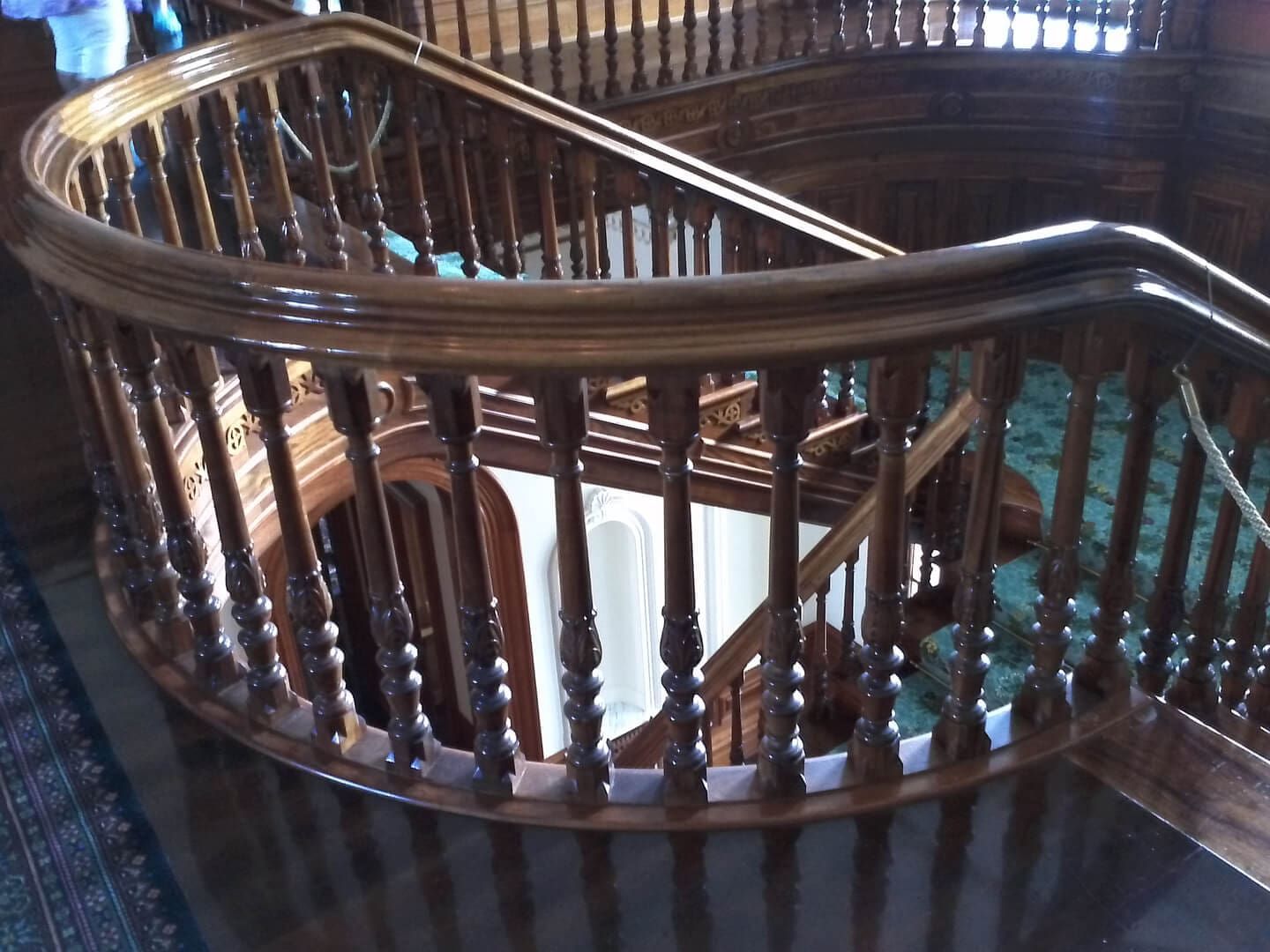 Wooden curved staircase with balusters and a dark glossy finish.