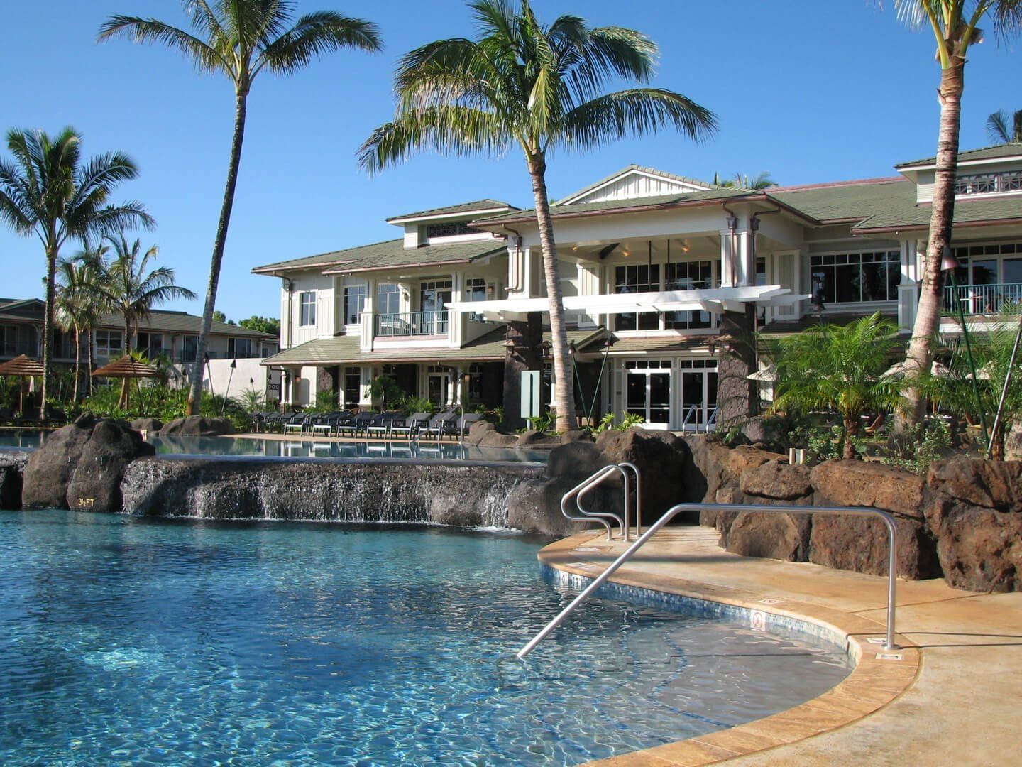 Luxury resort with pool and waterfall, palm trees, and multi-story buildings, sunny day.
