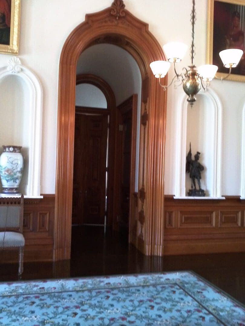 Ornate wooden doorway with arched frame. Detailed wood paneling and chandelier.