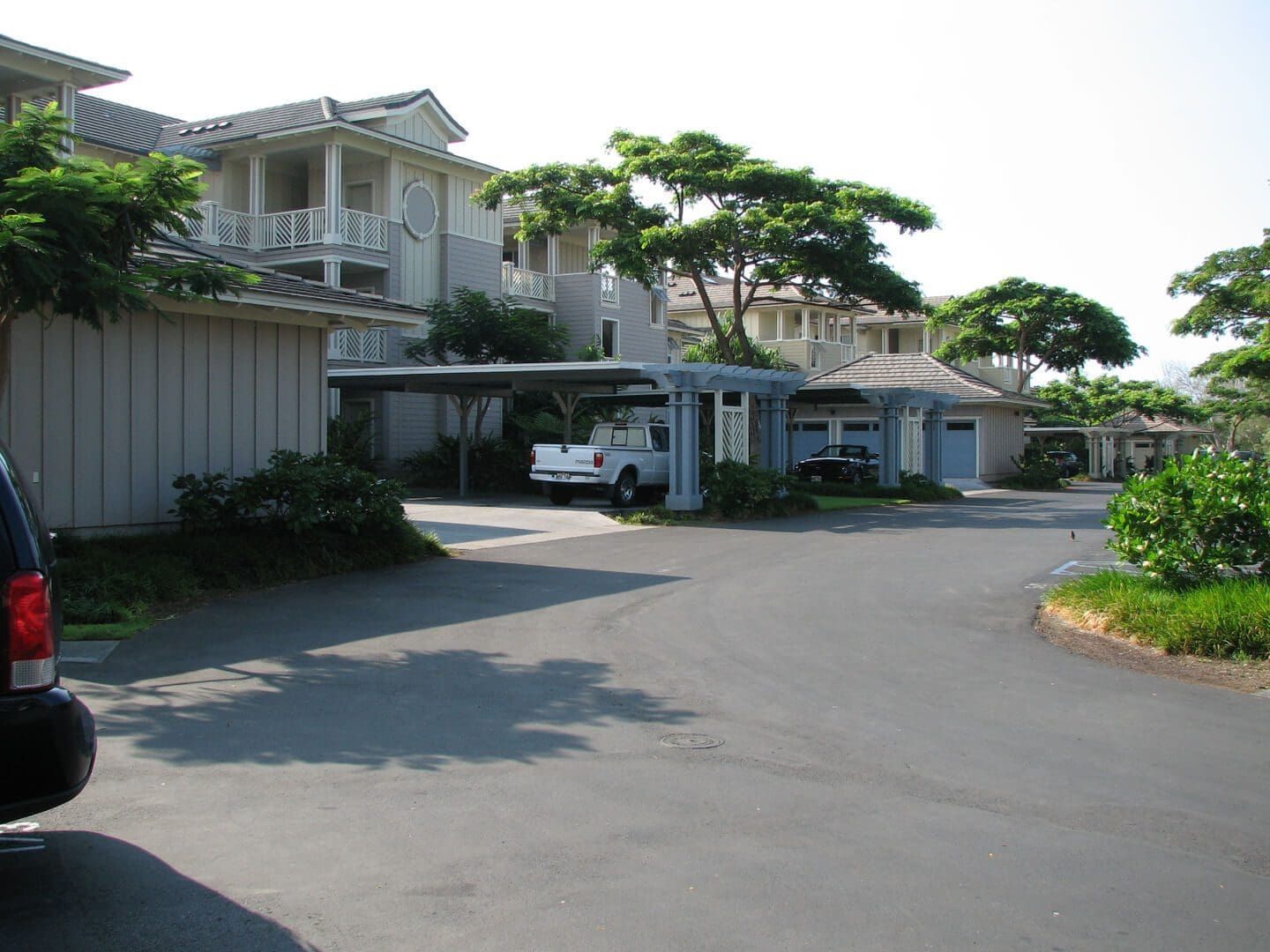 Paved road curving through a complex of light blue buildings with carports. A white pickup truck is parked under one.
