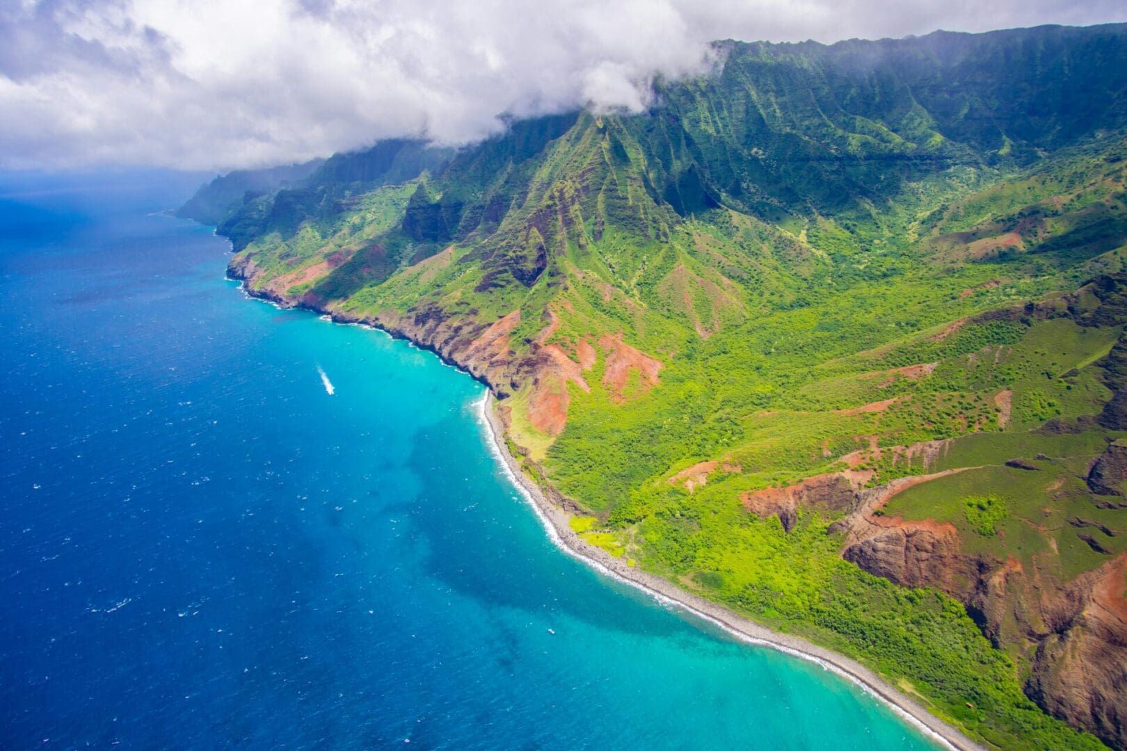 Ocean meets lush green cliffs on a coastline. Overcast sky.