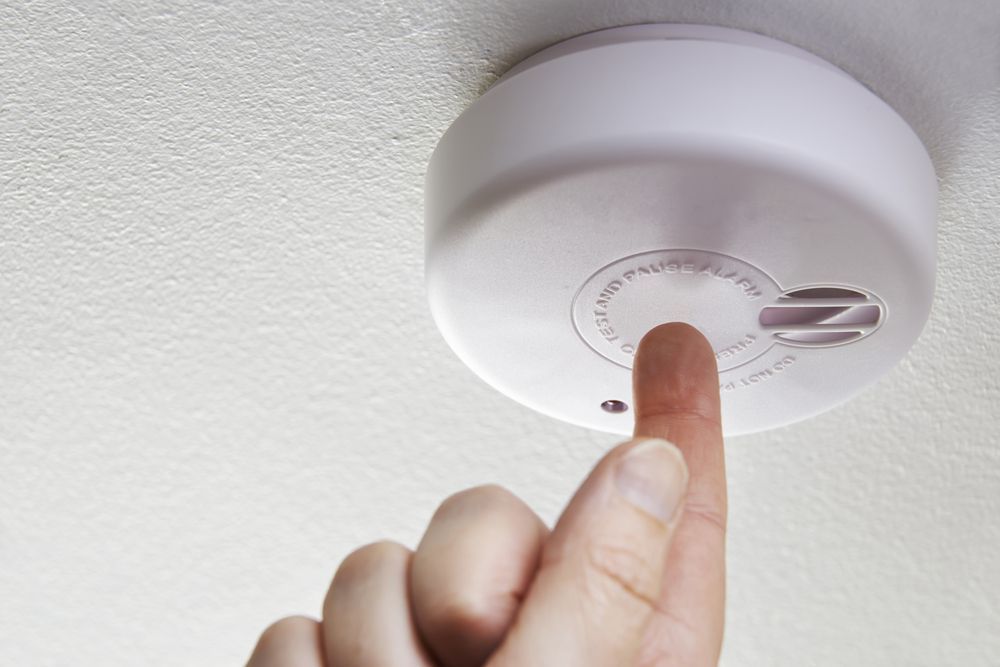 Close Up Of Hand Testing Domestic Smoke Alarm — Your Go-To Residential Electrician in Townsville, QLD