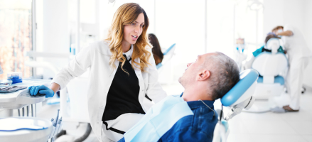 A dentist is talking to a patient in a dental chair about dental bridges.