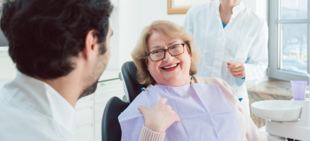 A woman is sitting in a dental chair talking to a dentist about dentures.
