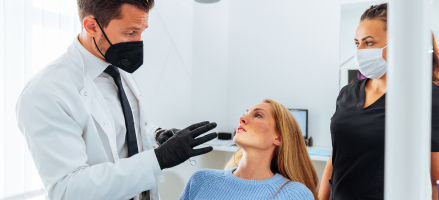 A dentist wearing a mask and gloves is explaining tooth extraction treatment to a women.
