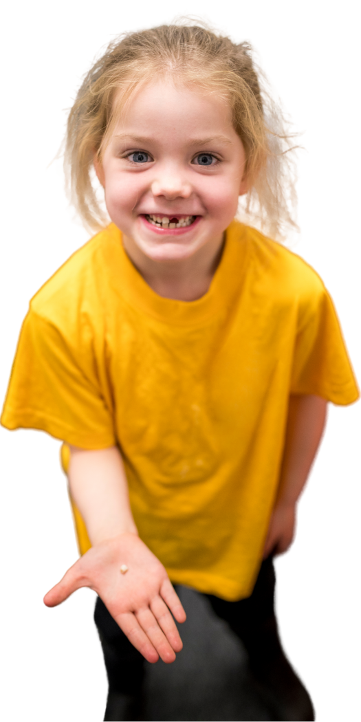 A little girl in a yellow shirt is smiling and holding out her hand with a tooth on it.