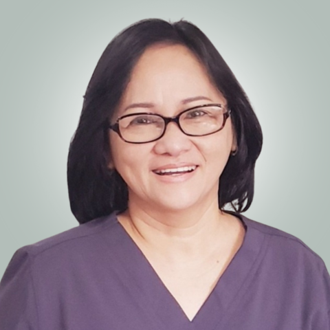 A woman wearing glasses and a purple scrub top is smiling.