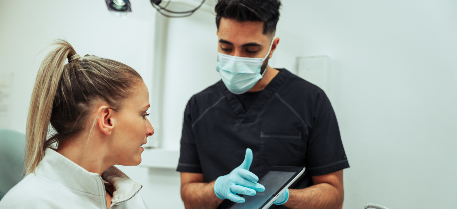 A dentist is talking to a patient in a dental office while looking at a tablet and explaining Sedation dentistry.