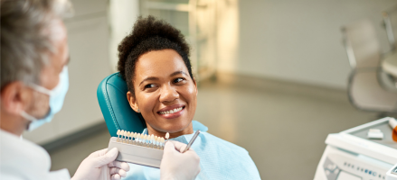 A woman is sitting in a dental chair while a dentist explains teeth veneers.