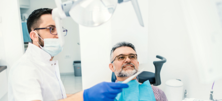 A dentist is pointing at a monitor consulting on a man 's teeth.