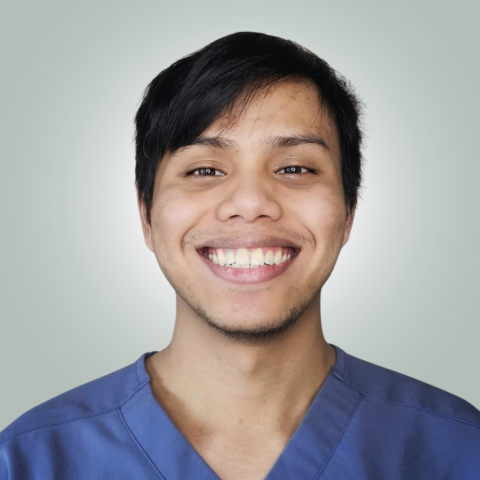 A man in a blue scrub top is smiling for the camera