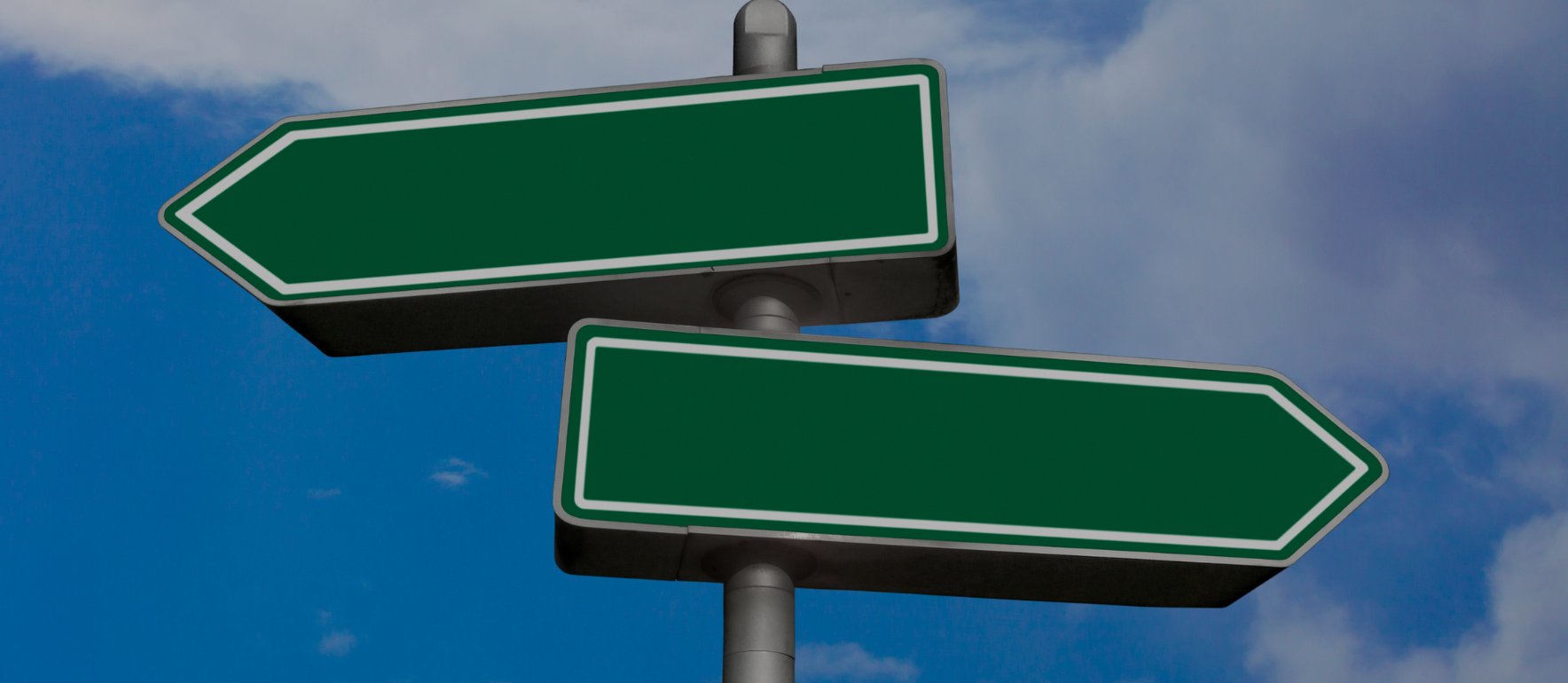 Two blank dark green signboards with white outlines point in opposite directions against a blue, cloudy sky.