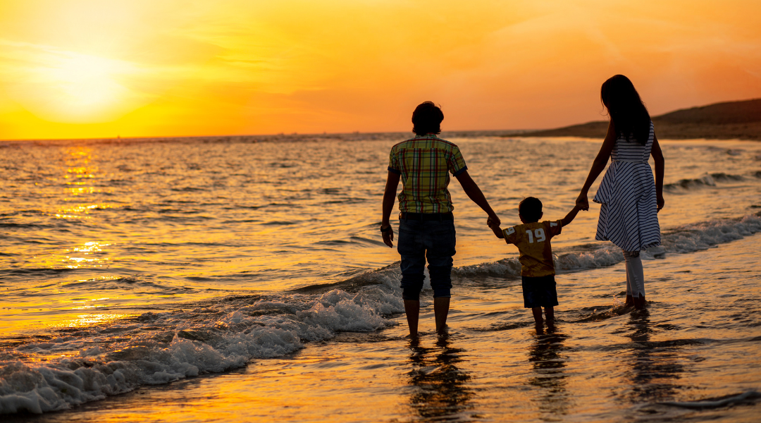 A family is walking on the beach at sunset holding hands.