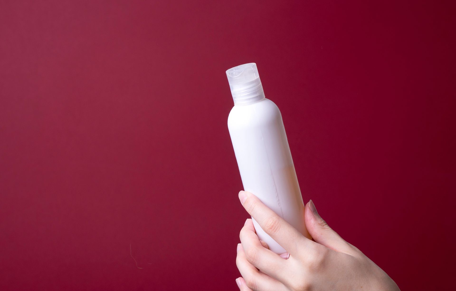Una mano che tiene una bottiglia bianca con tappo a scatto su sfondo rosso.