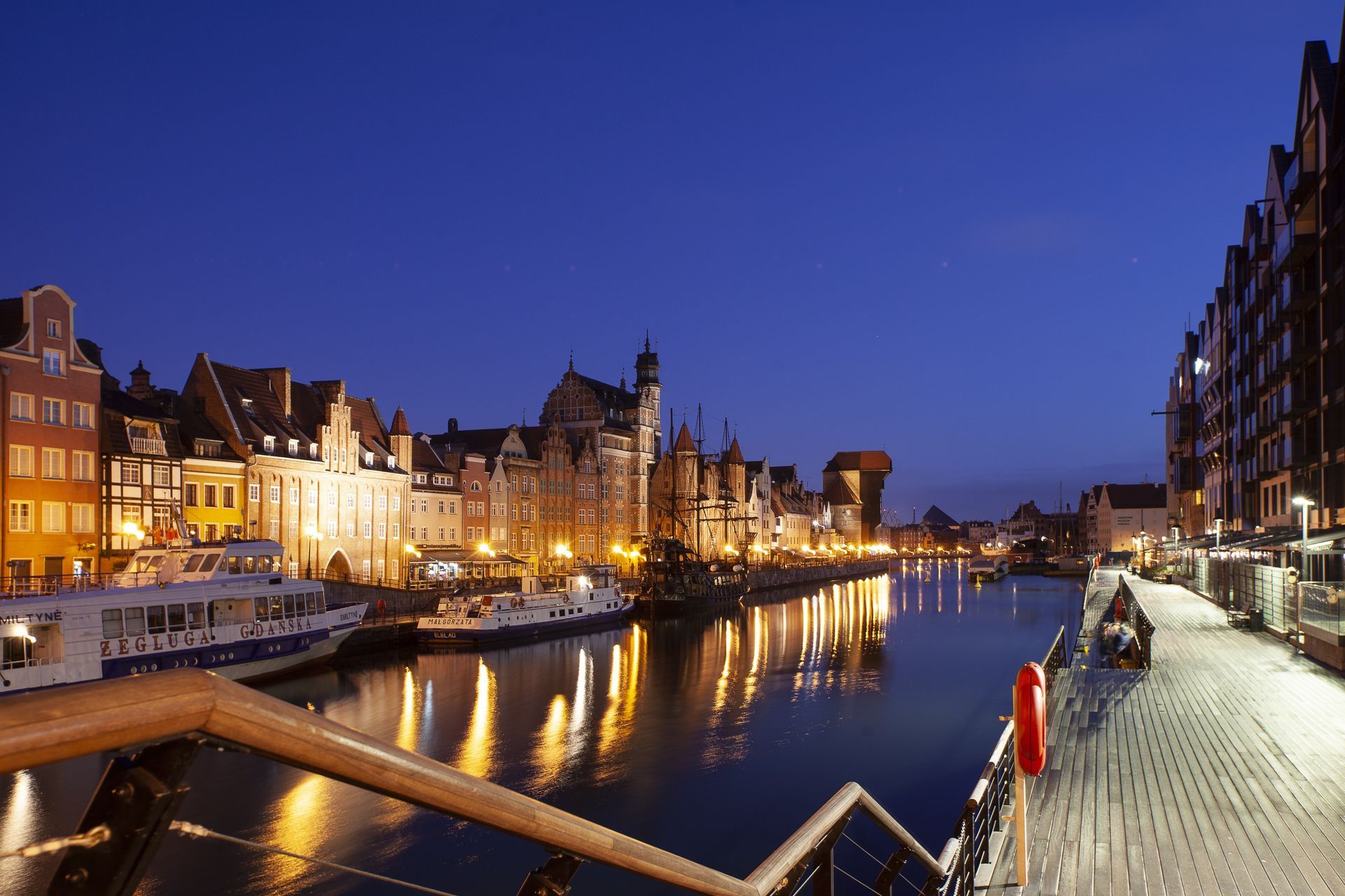 Gdańsk Old Town waterfront at night — colorful historic buildings reflected in the Motława River
