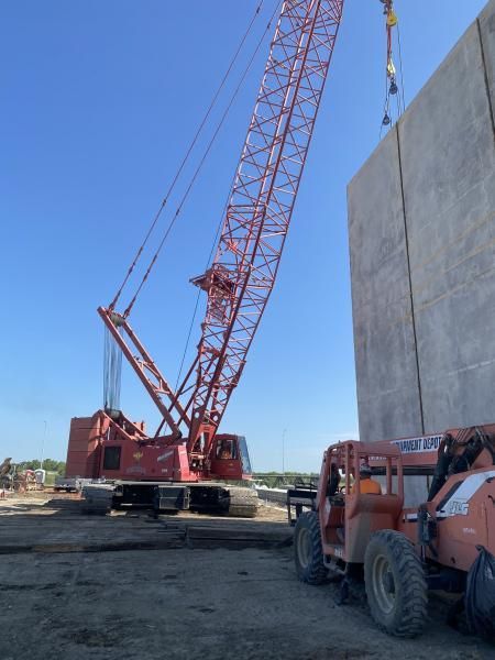 Large red crane at a construction site beside a concrete wall under a clear blue sky.
