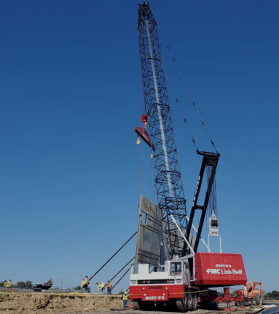 Blue-and-red crane lifting a worker at a construction site under a clear sky
