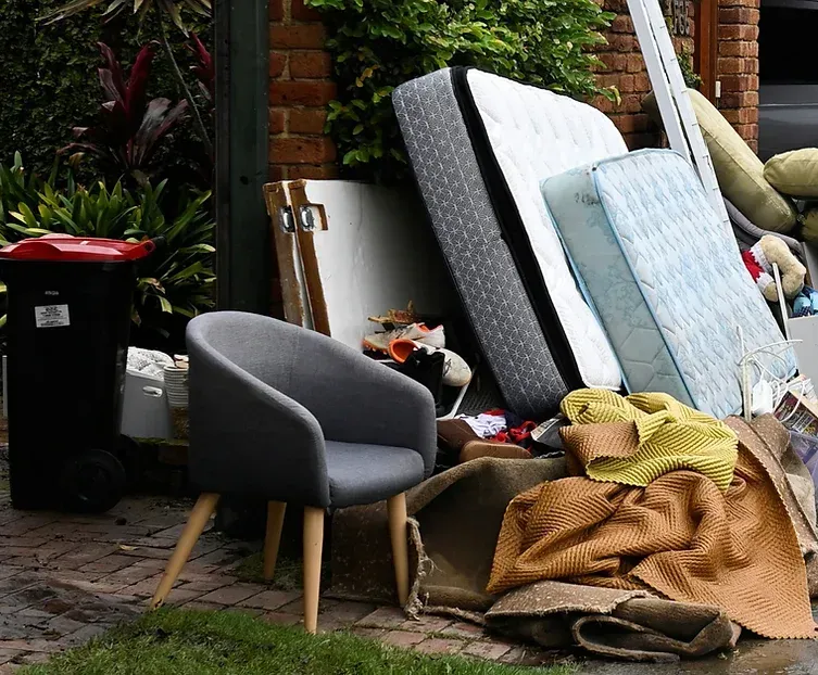 Damaged furniture and debris piled outside a brick house.