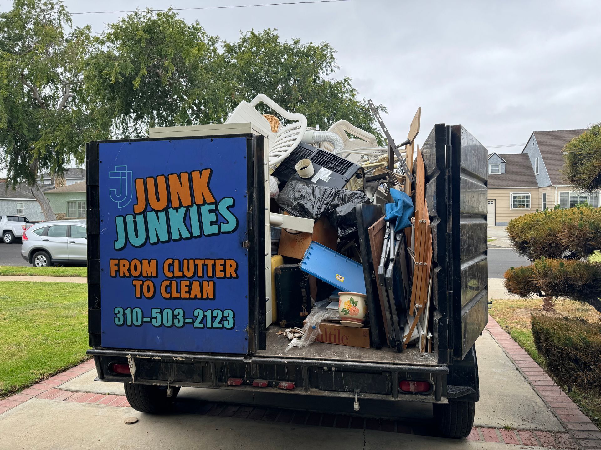 Junk removal truck loaded with debris in a suburban driveway, with