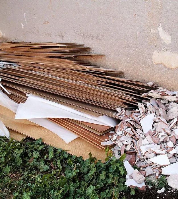 Piled cardboard sheets and broken white tile debris leaning against a wall outdoors