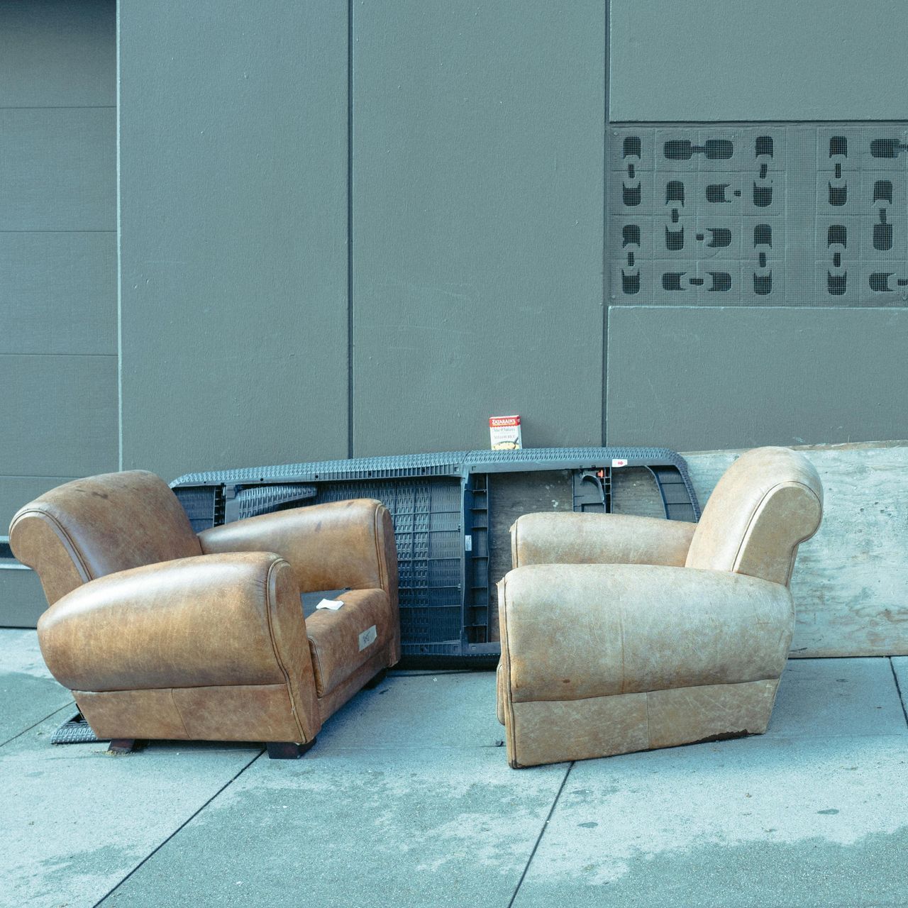 Two worn beige armchairs around a blue outdoor table against a gray wall