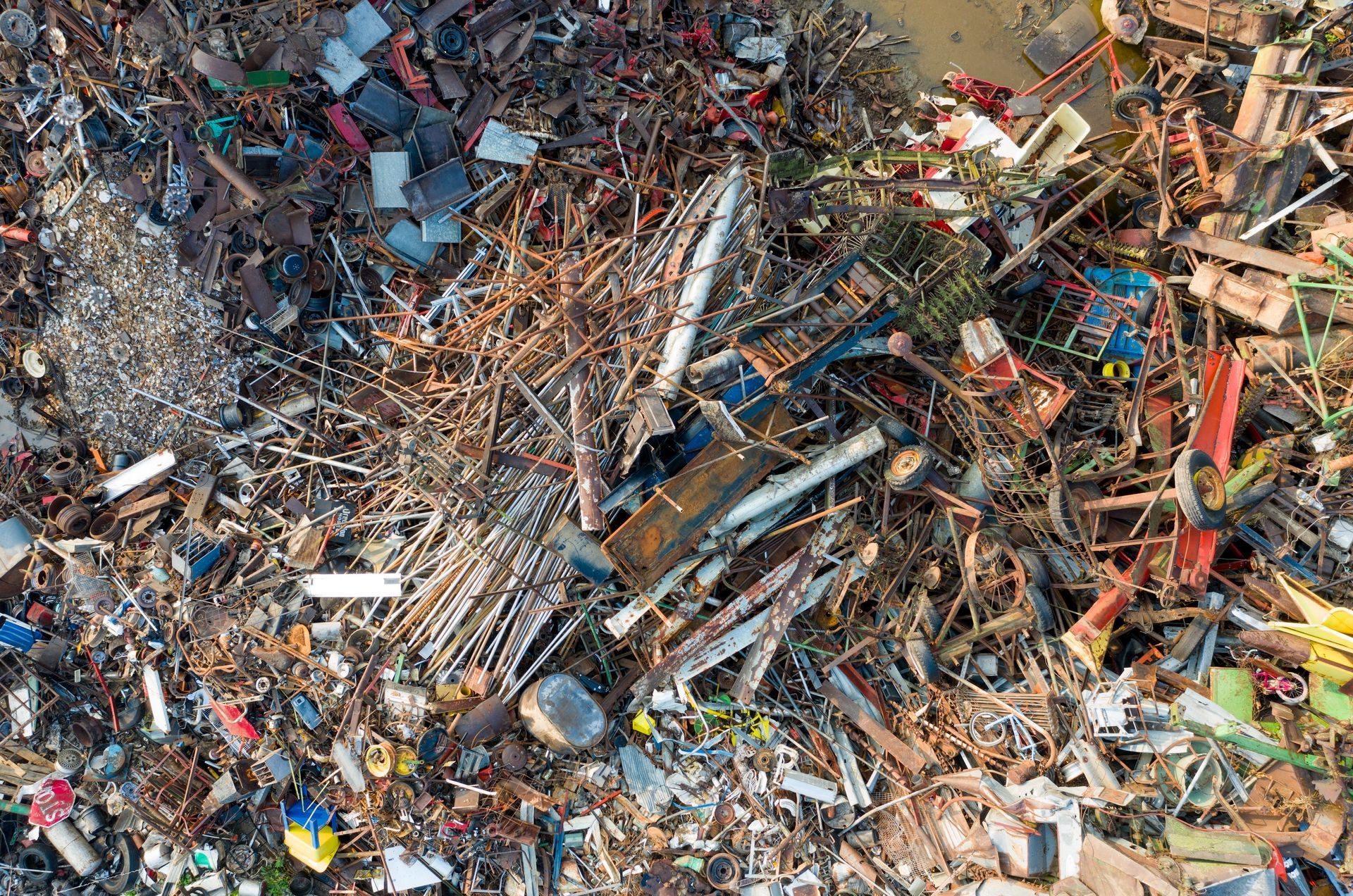 Aerial view of a large junkyard with piles of scrap metal, broken wood, and mixed debris.