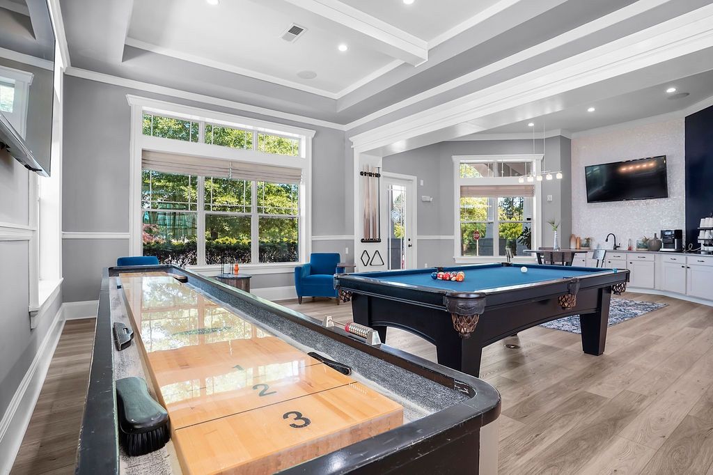 Interior community recreation room with a pool table, shuffleboard, lounge chairs, and large windows