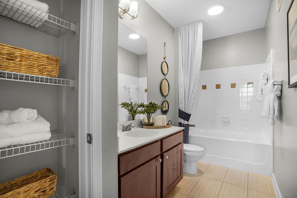 Bathroom featuring a vanity with sink, mirror, toilet, tub/shower, and open linen closet.