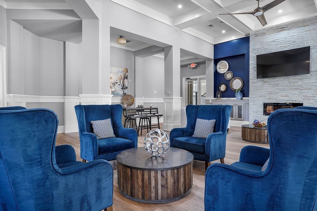 Communal lounge with blue velvet chairs around a round coffee table, fireplace, and TV.