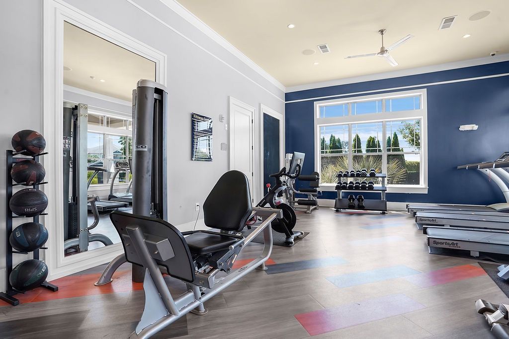 Interior gym with cardio machines, weights, and a large window.