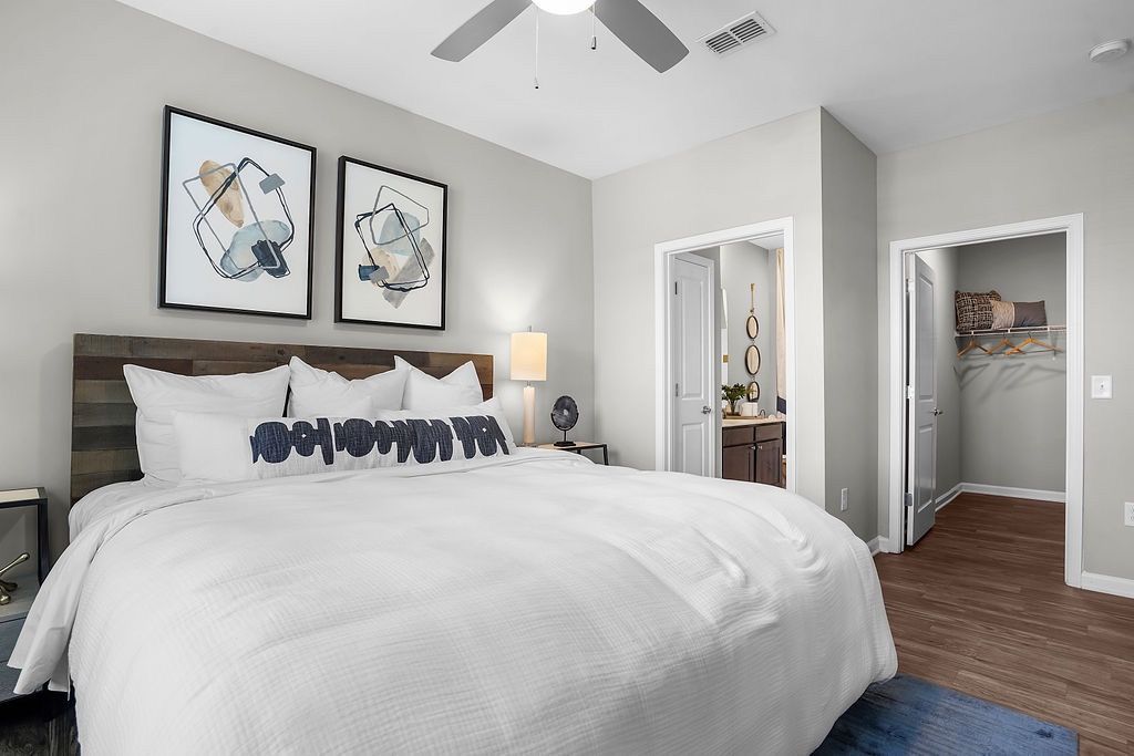 Bedroom with a large white bed, abstract art above, ceiling fan, and doors to bathroom and closet.