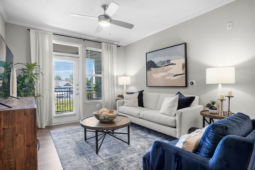 Bright apartment living room with white sofa, blue armchair, coffee table, and glass doors to balcony.