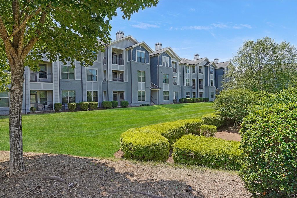 Exterior view of a multi-building apartment complex with a lush green lawn and trimmed shrubs.