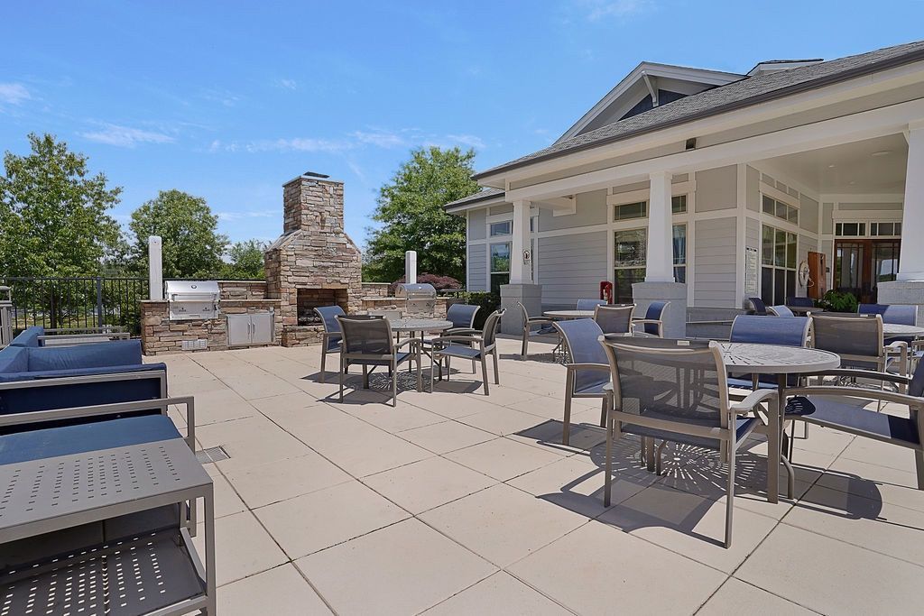 Outdoor community patio with tables, chairs, and a built-in grill beside a clubhouse.