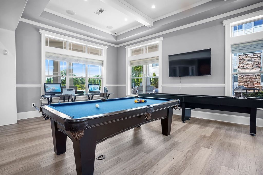 Indoor community recreation room with a pool table and a wall-mounted TV beside large windows.