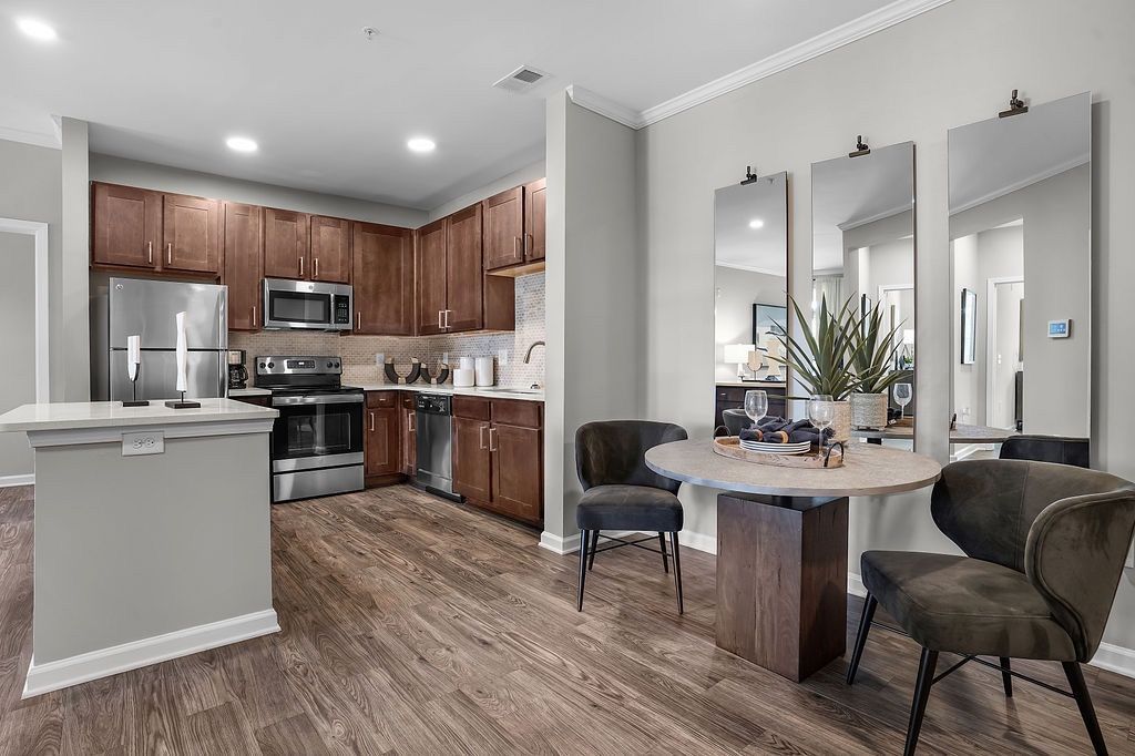 Open-concept apartment kitchen with dark wood cabinets, stainless-steel appliances, and a round dining table.