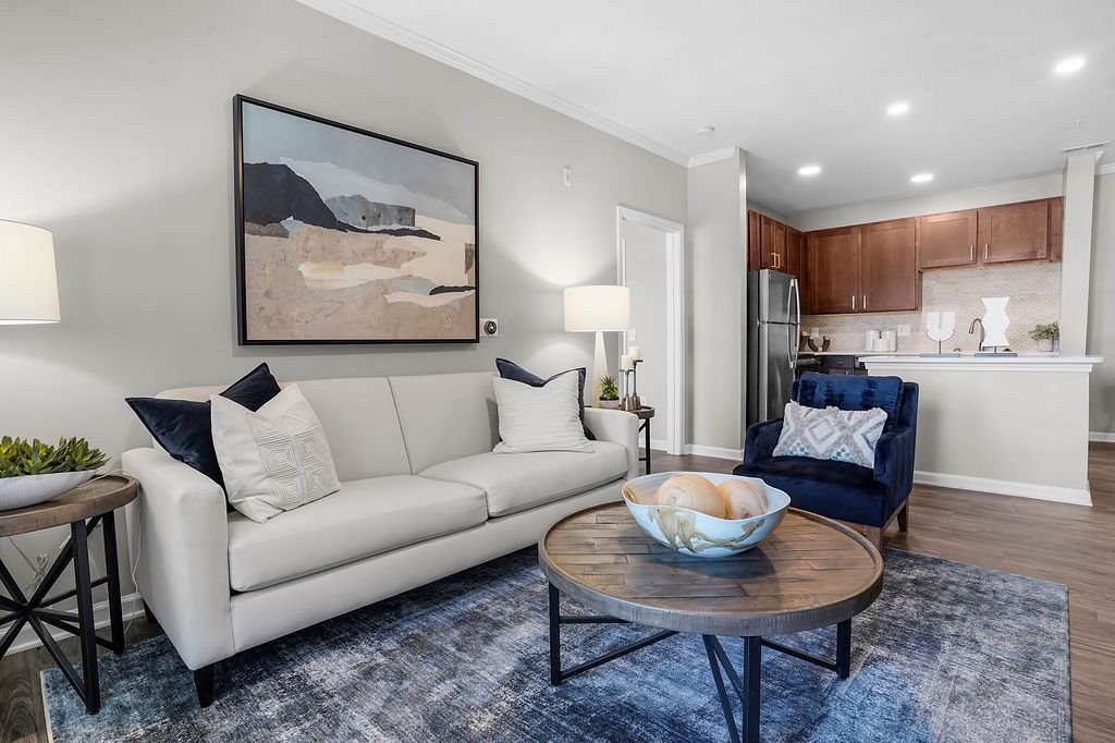 Bright apartment living room with a white sofa, navy armchair, round wood coffee table, and an open kitchen.
