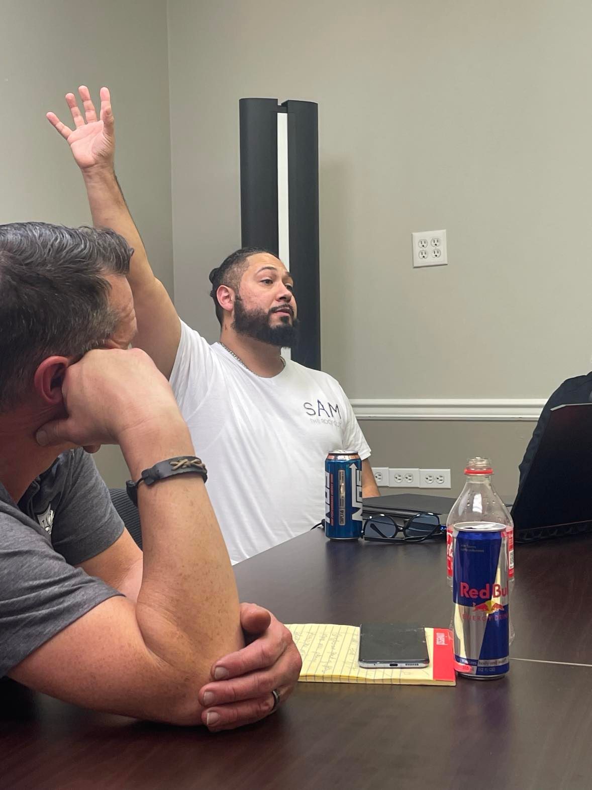 A man is sitting at a table with his hand up.