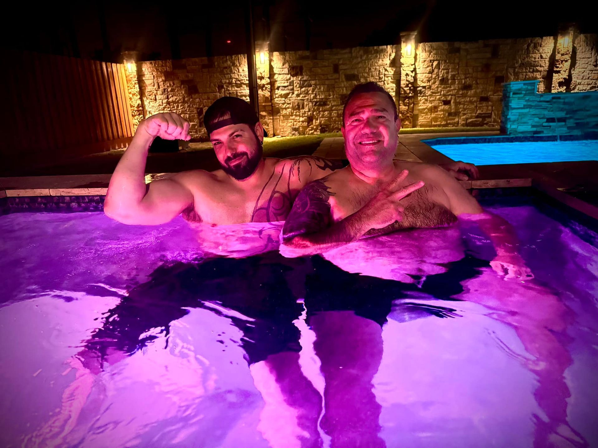 Two men are sitting in a swimming pool with purple lights.