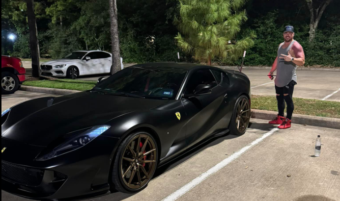 A man is standing next to a black ferrari in a parking lot.