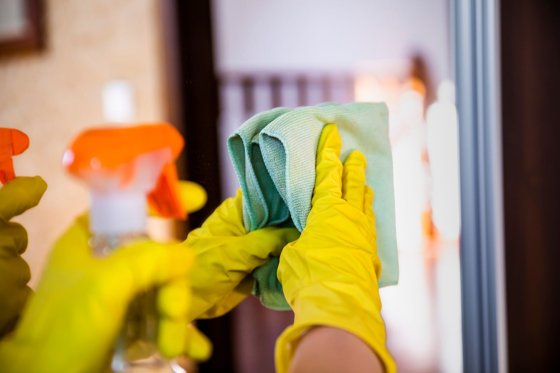 A person wearing yellow gloves is cleaning a mirror with a cloth.