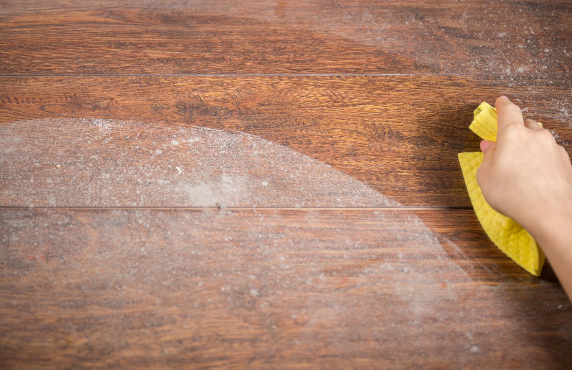 A person is cleaning a wooden table with a yellow cloth.