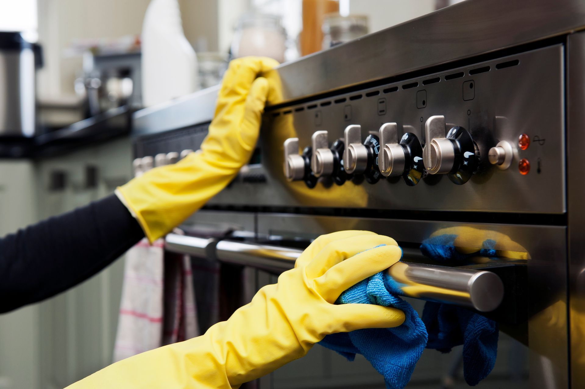 A person wearing yellow gloves is cleaning a stove with a cloth.