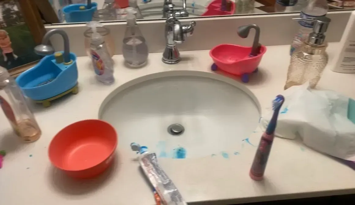 A bathroom counter with a sink , bowls , toothbrushes and soap