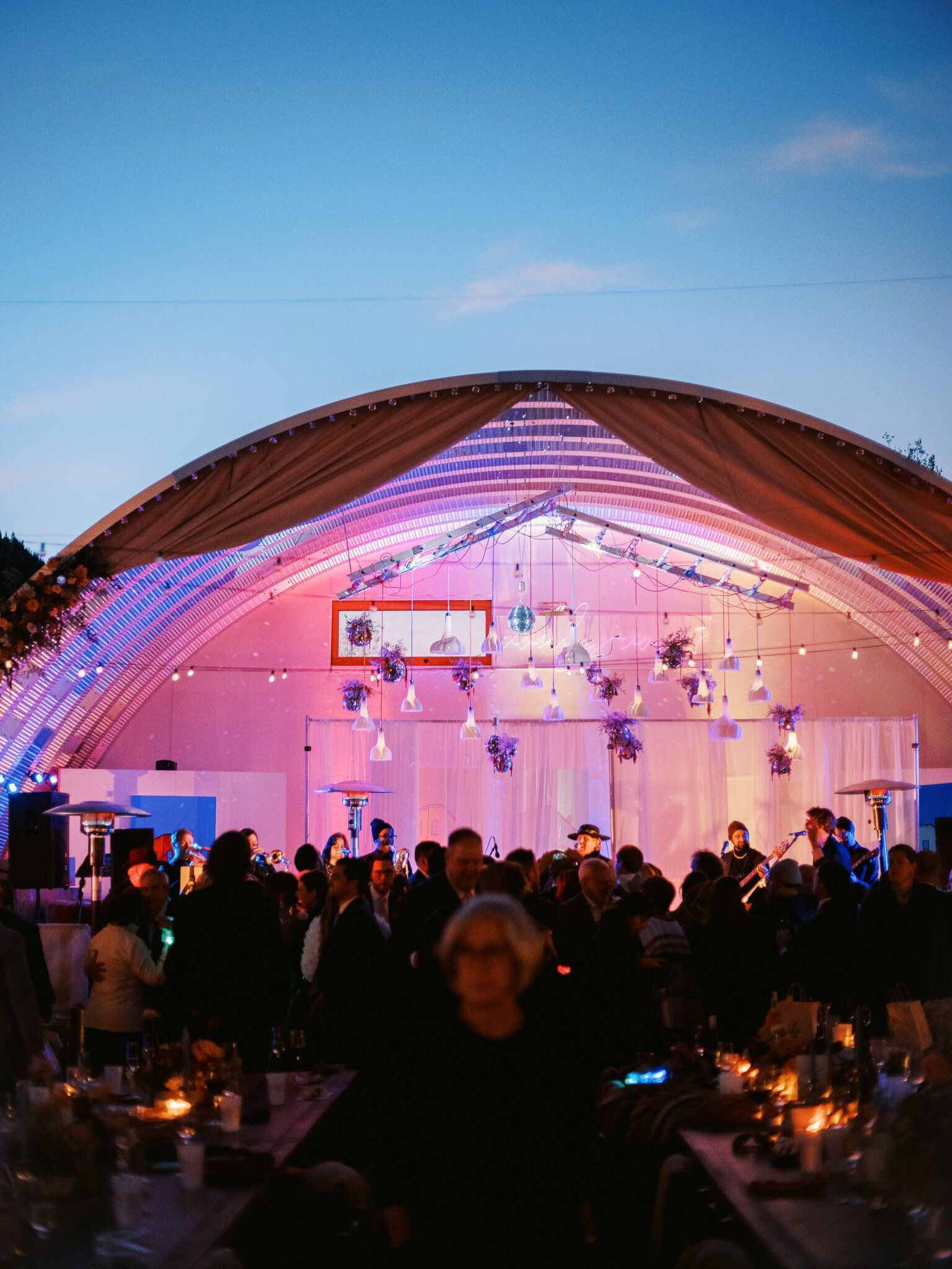 A crowd of people are gathered under a tent at a party.