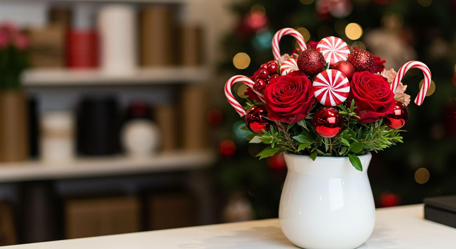 Christmas floral arrangement in white vase with red roses, candy canes, and ornaments.