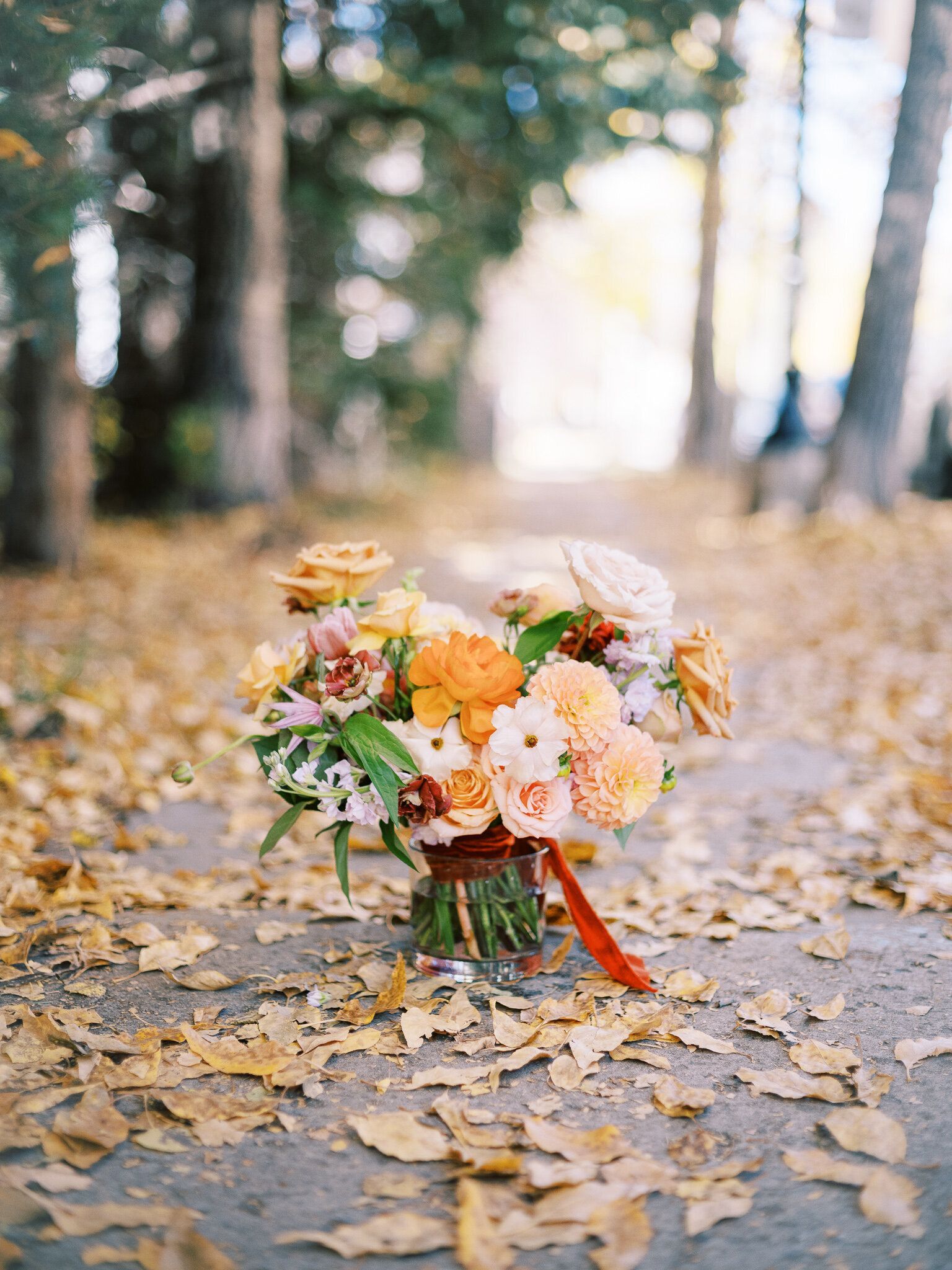 A bouquet of flowers in a vase sitting on top of a pile of leaves.